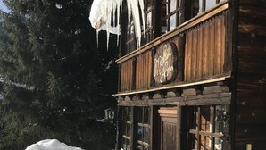 A wooden building with icicles hanging from the roof, surrounded by snow and trees.
