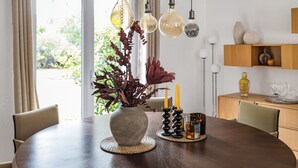 Una mesa redonda de comedor con un jarrón de plantas secas, velas y un recipiente de vidrio.