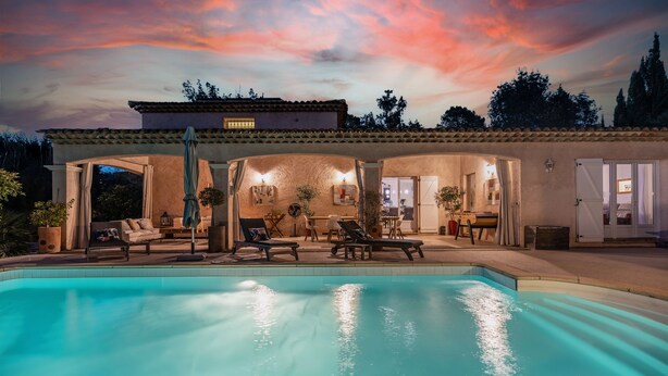 Un área junto a la piscina con sillones de descanso, una mesa de comedor y un porche cubierto.