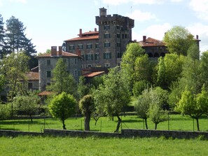 Eine steinerne Burg mit einem Turm, umgeben von üppiger Vegetation und Bäumen.