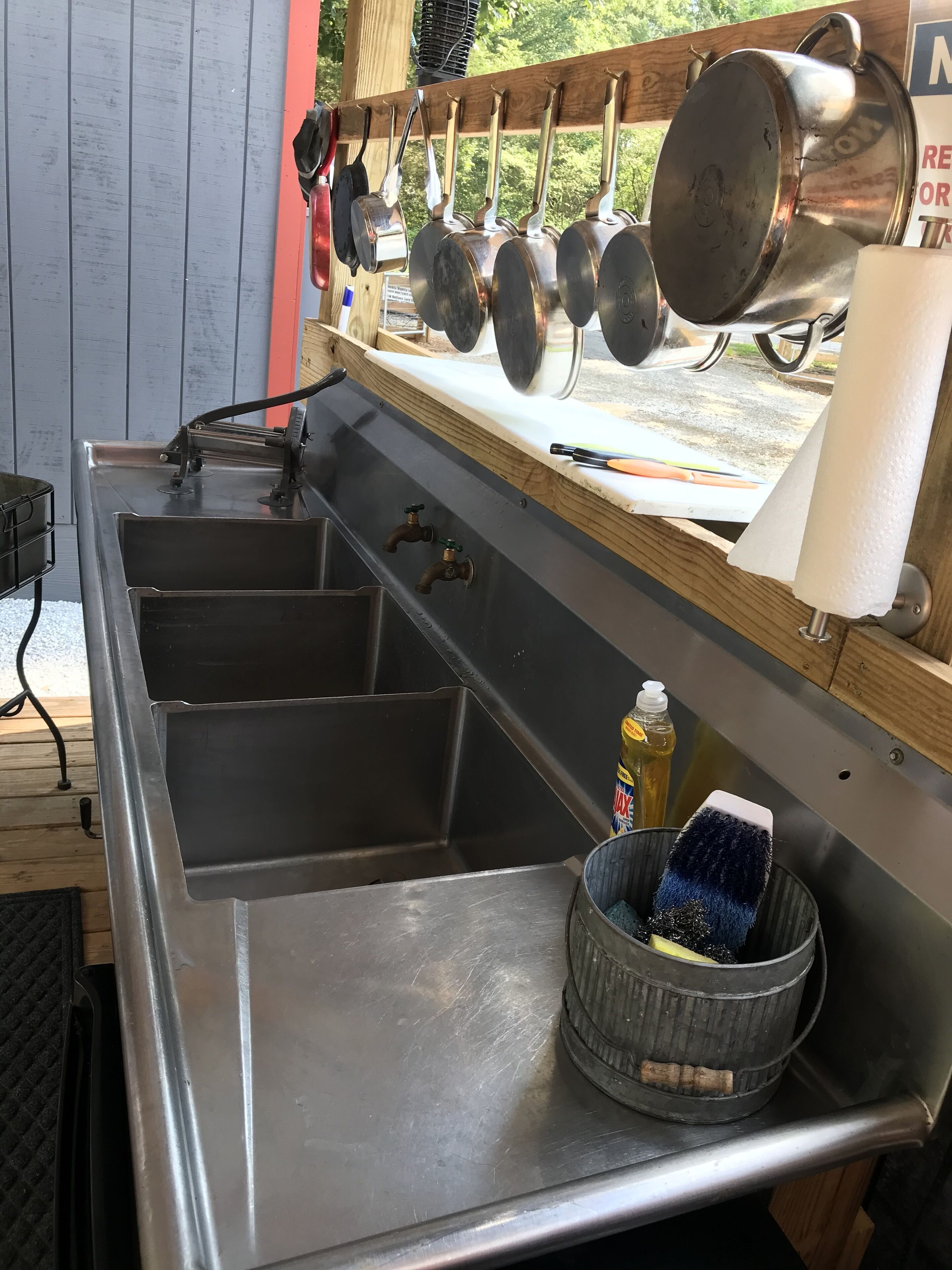 A stainless steel kitchen with multiple sinks, hanging pots, and a dish soap bottle.