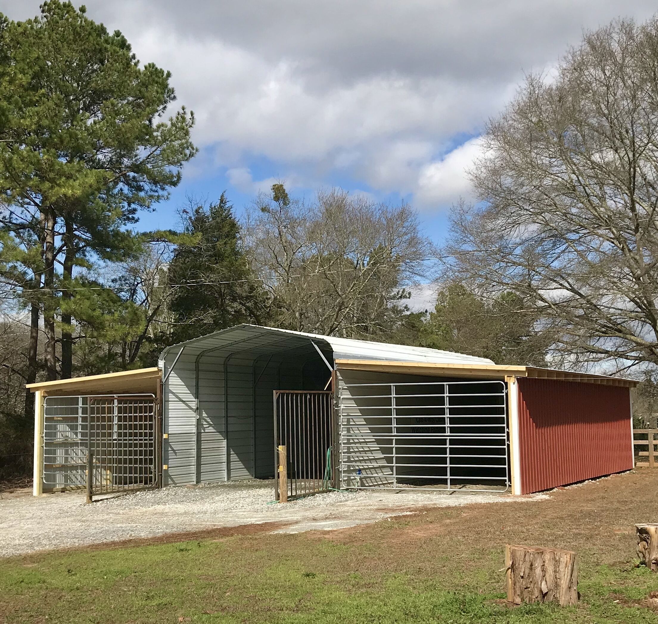A metal barn with a covered entrance and a fenced area.