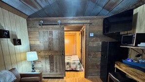 Una habitación acogedora con suelo de madera, un sofá, una mesa con microondas y un televisor en la pared.