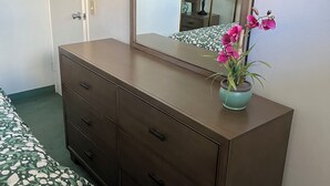 Een slaapkamer met een houten dressoir, een bed met bloemenbeddengoed, een spiegel en een potorkidee.