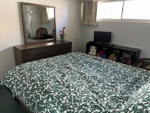 A bedroom with a bed, dresser, mirror, and a television on a stand.