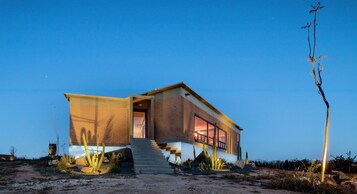 Una casa moderna con un gran ventanal, una escalera y un paisaje desértico.