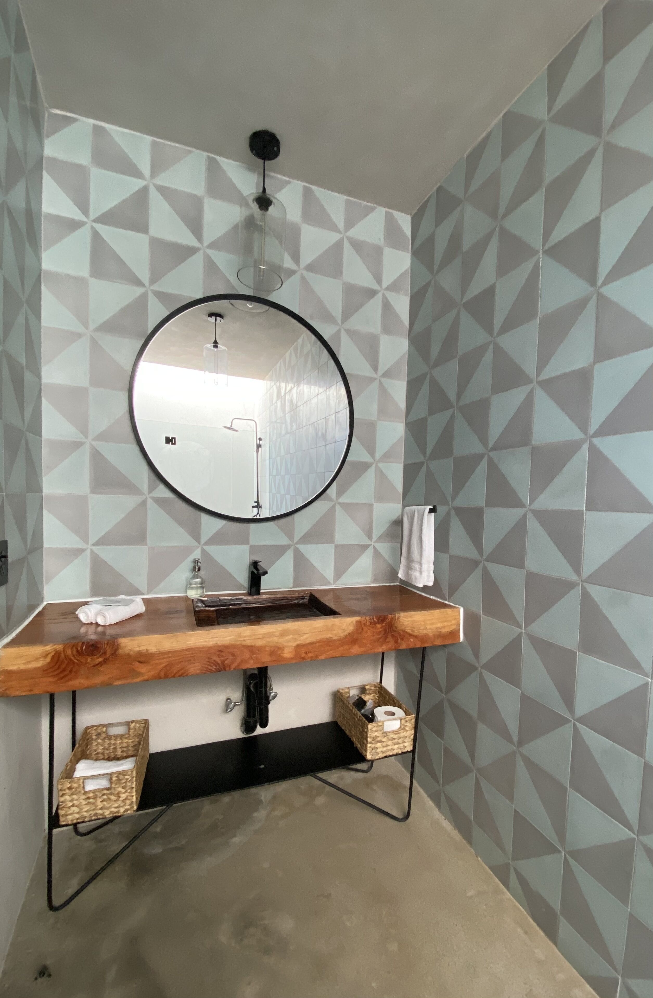 A bathroom with a round mirror, wooden vanity, and geometric-patterned walls.