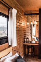 Un baño con pared de ladrillo, encimera de madera y espejo. Se ven botellas y un perchero para toallas.