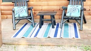 A wooden cabin with two rocking chairs and a small table, each with a turtle-themed pillow. - Glacier Lake Log Cabin (Oxford)