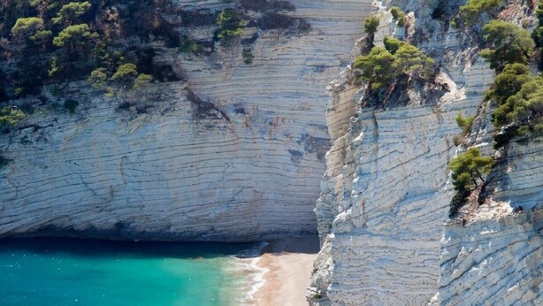 Une falaise côtière avec une plage et des eaux turquoise.