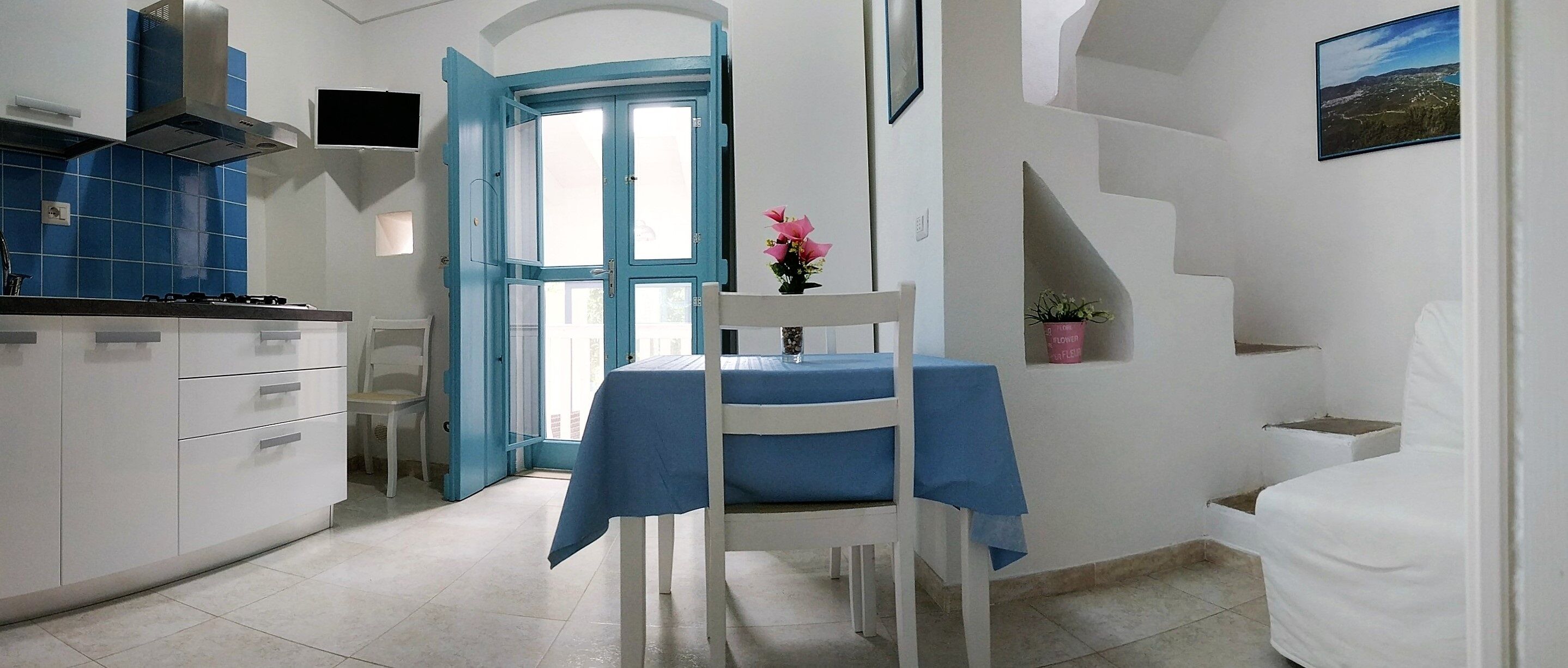 Una cocina compacta con una puerta azul, armarios blancos y una mesa de comedor con mantel azul.