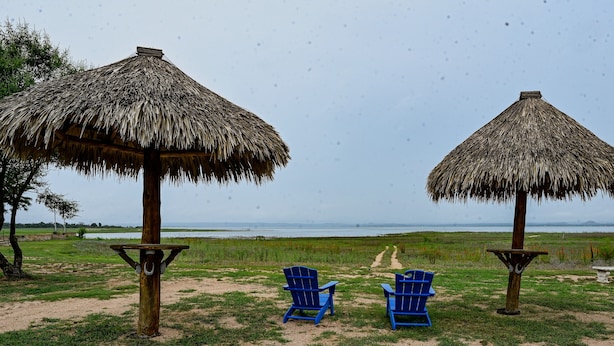Two thatched-roof structures with blue chairs in front, a dirt path, and a view of the water. - Small but cozy apartment style lakefront home on Buchanan Dam with great views! (Buchanan Dam)