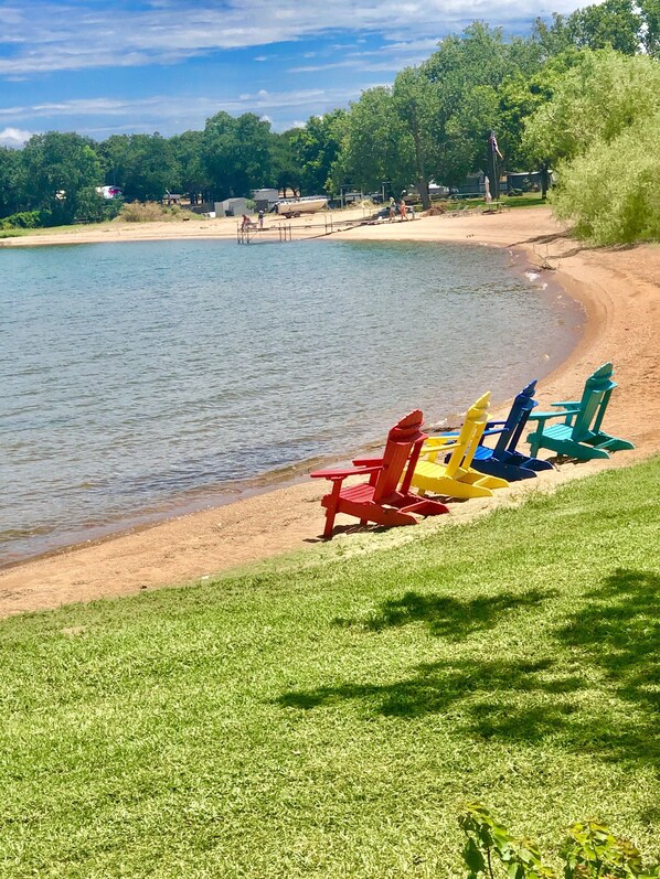 Vista al lago con zona de césped y coloridas sillas Adirondack a lo largo de la orilla.