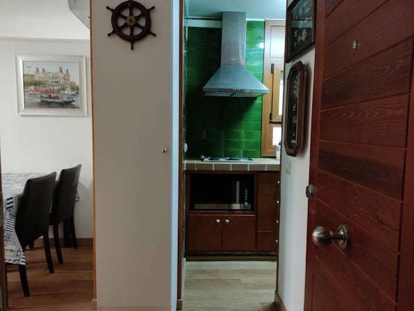 A narrow hallway leading to a kitchen with a green backsplash, a stainless steel range hood, and wooden cabinets.