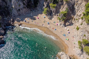 An aerial view of a beach with clear turquoise waters, rocky cliffs, and numerous beach umbrellas.