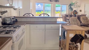 Una cocina con estufa a gas, tostadora y vista al océano a través de amplios ventanales.