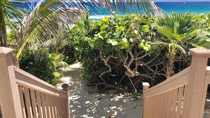Una escalera de madera que baja a una playa arenosa con vegetación tropical y vistas al océano.