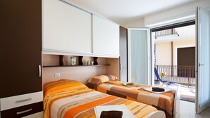 Ein Hotelzimmer mit zwei Betten, einem Kleiderschrank, einem Balkon mit einem Stuhl und Blick ins Freie.