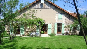A stone building with a sloped roof, green shutters, and a satellite dish.