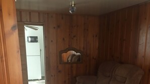 Ein Zimmer mit Holzwänden, einem braunen Ledersofa, einer gemusterten Bettdecke und einem Deckenventilator.