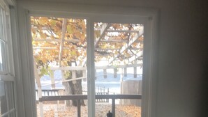 Ein Essbereich mit Tisch und vier Stühlen, ein Fenster mit Blick auf eine Holzterrasse und Bäume, sowie eine weiße Decke.