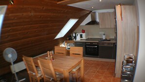 A kitchen with wooden cabinets, a dining table with chairs, a fan, and a window. - Feel-good nest with children's bunk (Dornum OT Dornumersiel)