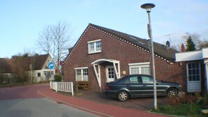 A brick building with a car parked in front, a red sidewalk, and a street sign. - Feel-good nest with children's bunk (Dornum OT Dornumersiel)