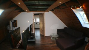 An attic room with a wooden ceiling, a dark brown sofa, a small glass table, and a wooden staircase. - Feel-good nest with children's bunk (Dornum OT Dornumersiel)