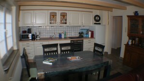Una cocina compacta con armarios blancos, un microondas y un fregadero. Hay una mesa de comedor con sillas y un libro encima.