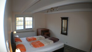 Un dormitorio con una cama, una mesita de noche, una lámpara, una ventana y un espejo en la pared.