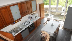 A modern kitchen with wooden cabinets, a gas stove, a microwave, and a dining area with a table and chairs. - JOY VILLA APARTMENT LOFT (Acqui Terme)