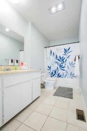 A bathroom with a white sink, mirror, and toilet. There is a shower curtain with a leaf pattern, a towel hanging on the wall, and a small rug on the floor. - 2330/B Comfy 2 bed dual master with Backyard! (San Diego)