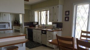 Une cuisine avec des meubles blancs, un four à micro-ondes, une machine à café et un coin repas comprenant des chaises et une table en bois.