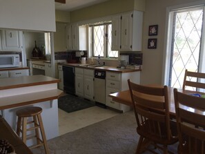 A kitchen with white cabinets, a microwave, a coffee maker, and a dining area with wooden chairs and a table.