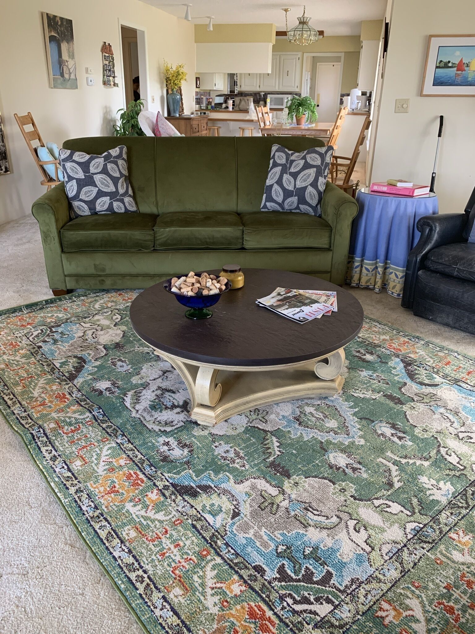 Una sala de estar con un sofá verde, una mesa redonda de centro con un cuenco de tapones de corcho, y una alfombra estampada.