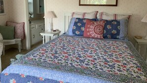 Une chambre à coucher avec une couvre-lit à motifs floraux, une table de chevet avec une lampe, une chaise et une commode.