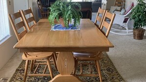 Une salle à manger avec une table en bois, des chaises et un tapis à motifs. On y trouve un ventilateur de plafond et un lustre.