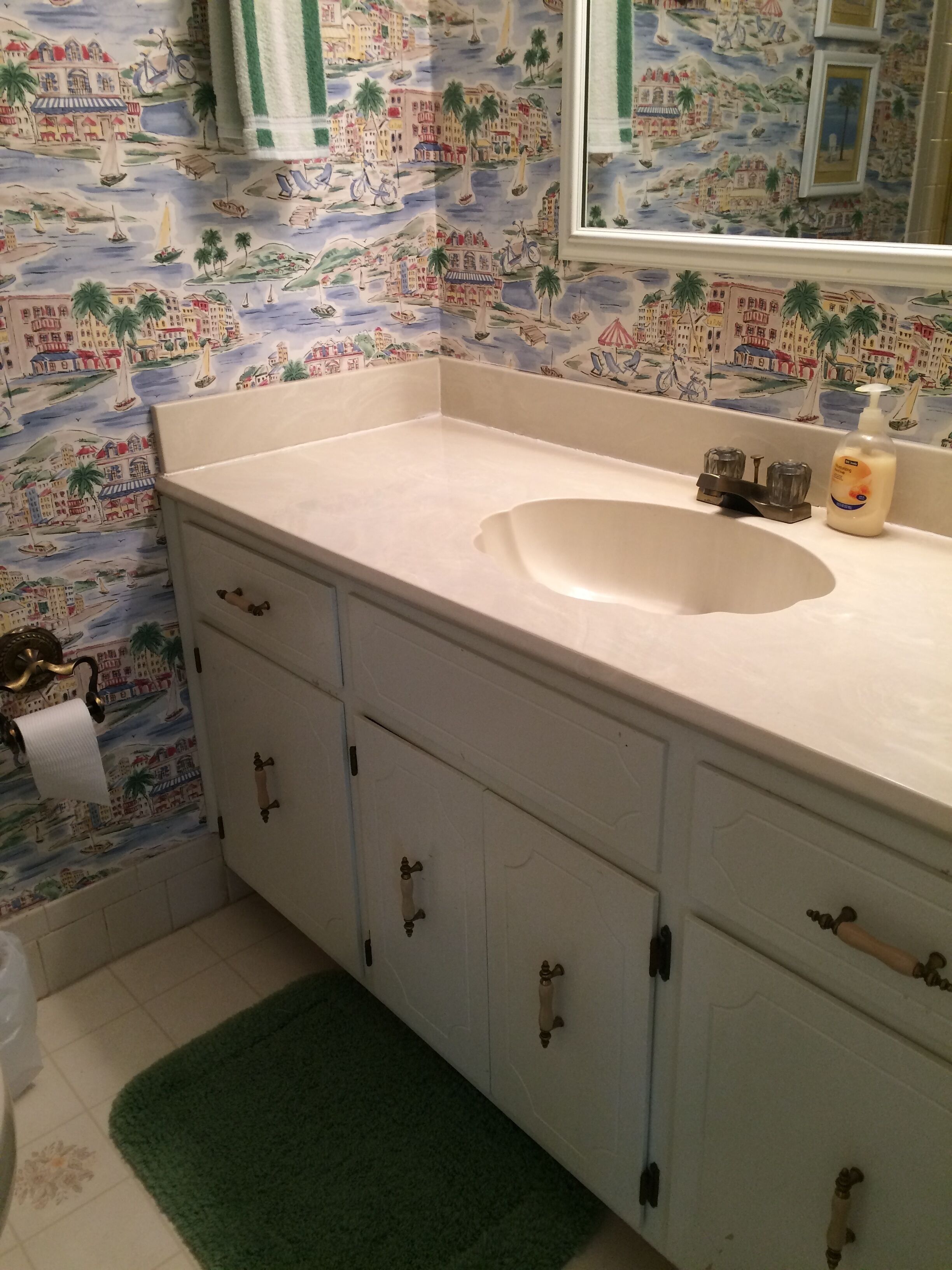 A bathroom with a white sink, a mirror, and a green rug.