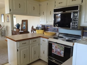 A kitchen with white cabinets, a stove, a microwave, and a refrigerator.