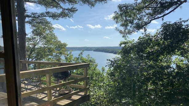 Une terrasse en bois avec une rambarde en métal, donnant sur un lac et entourée d’arbres.
