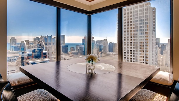 Ein stilvoller Essbereich mit großem Tisch und Stühlen, einer Blumenvase und Blick auf die Stadt durch große Fenster.