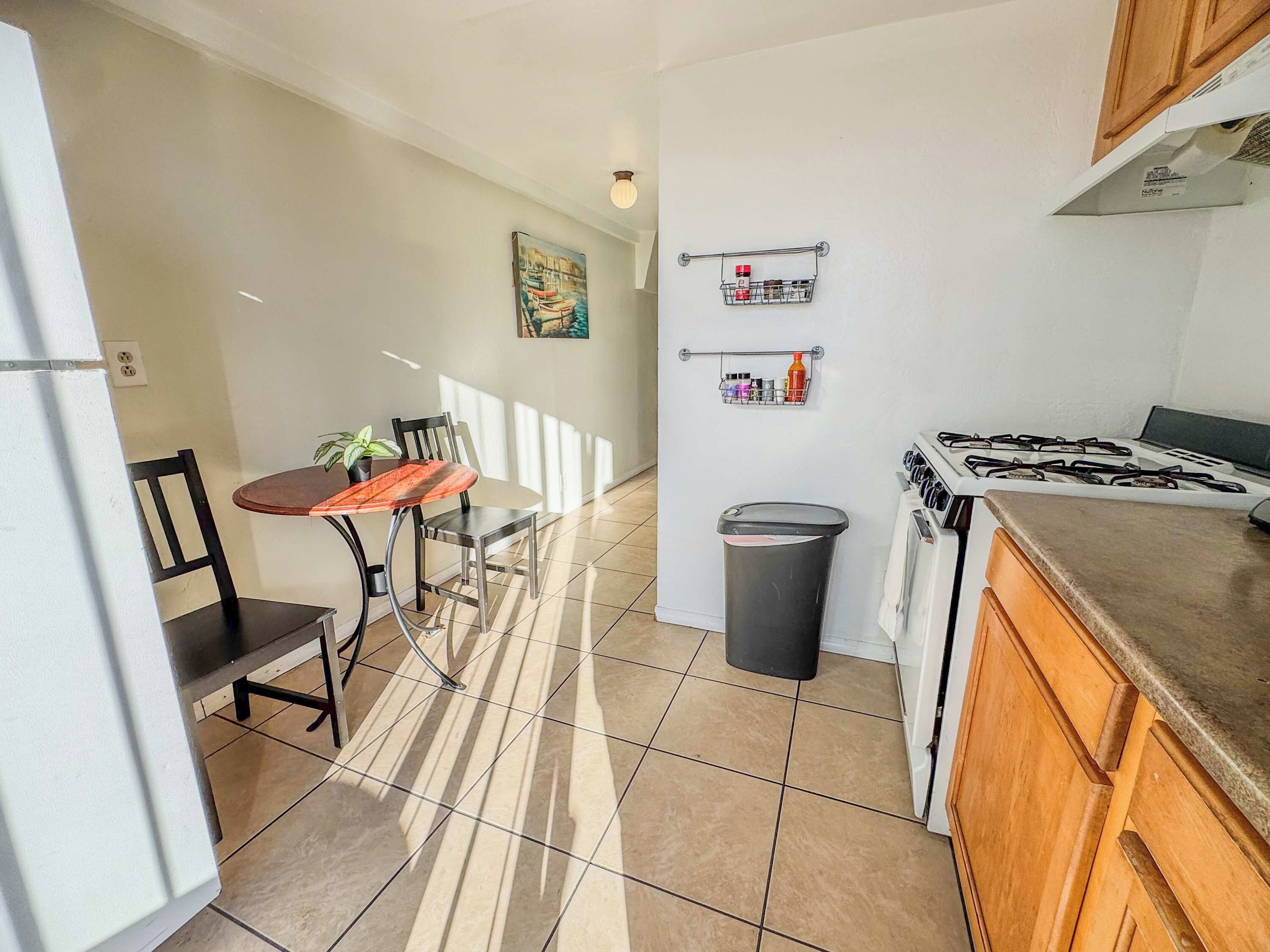 A compact kitchen with a dining area, a trash bin, and a gas stove.