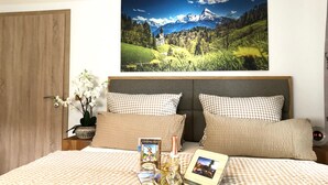 Camera d'albergo con un letto, cuscini a quadri, un comodino con una sveglia, un quadro incorniciato e una bottiglia di champagne.