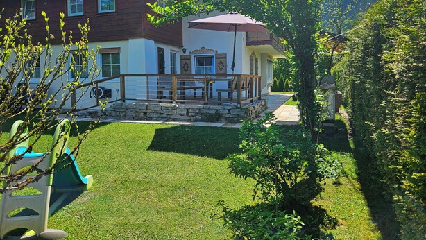 Una casa a due piani con fondamenta in pietra, un balcone con ringhiera in legno e un prato curato.