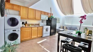 Cocina compacta con armarios de madera, microondas, refrigerador, lavadora y comedor con mesa y sillas.