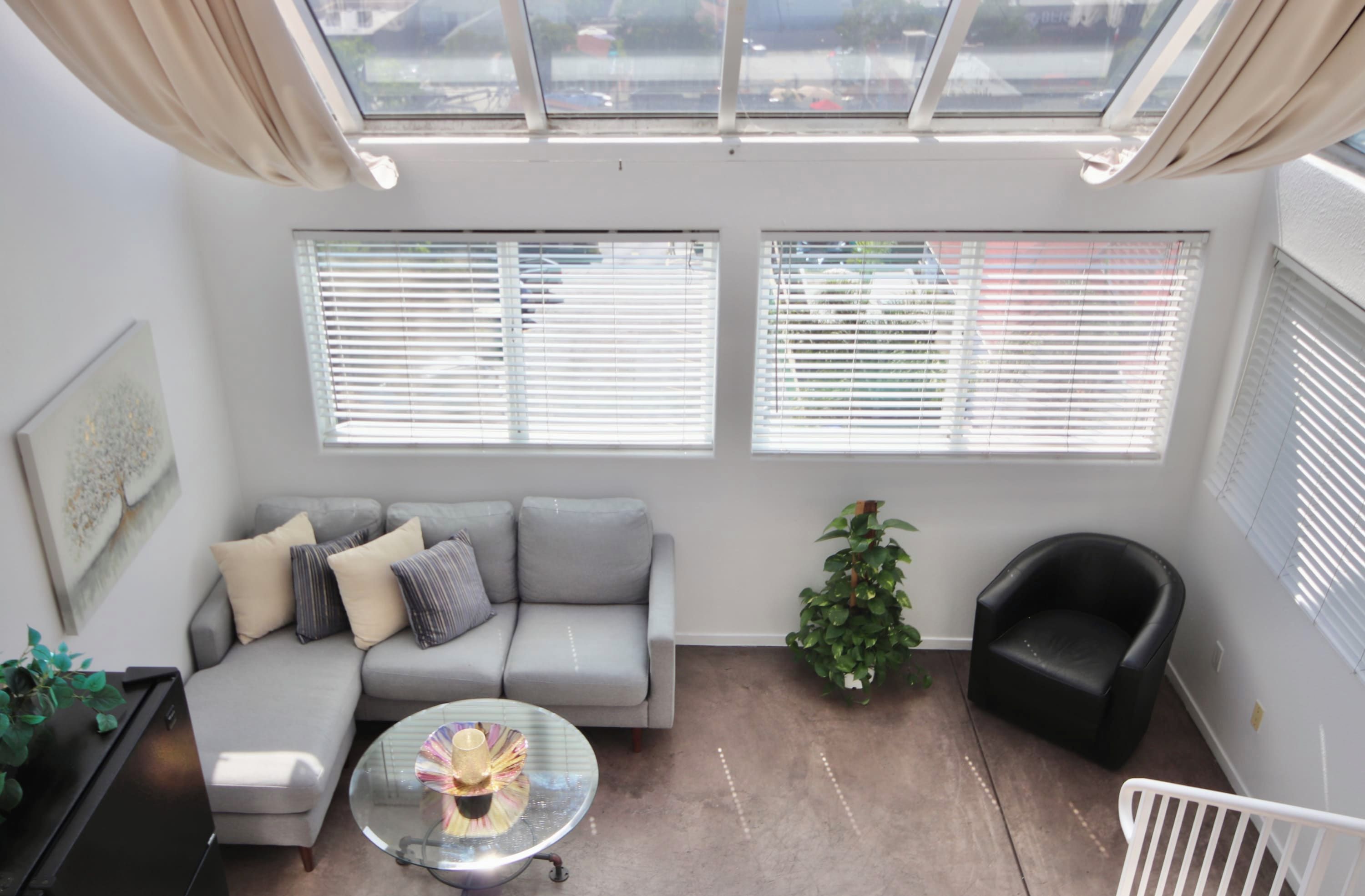 Una sala de estar moderna con un sofá seccional gris, una mesa de centro de vidrio, un sillón negro y una planta en maceta.