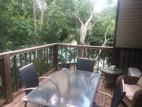 A wooden deck with a glass table and two wicker chairs, surrounded by trees.