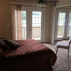 A bedroom with a bed, a chair, and a balcony with a wooden railing.