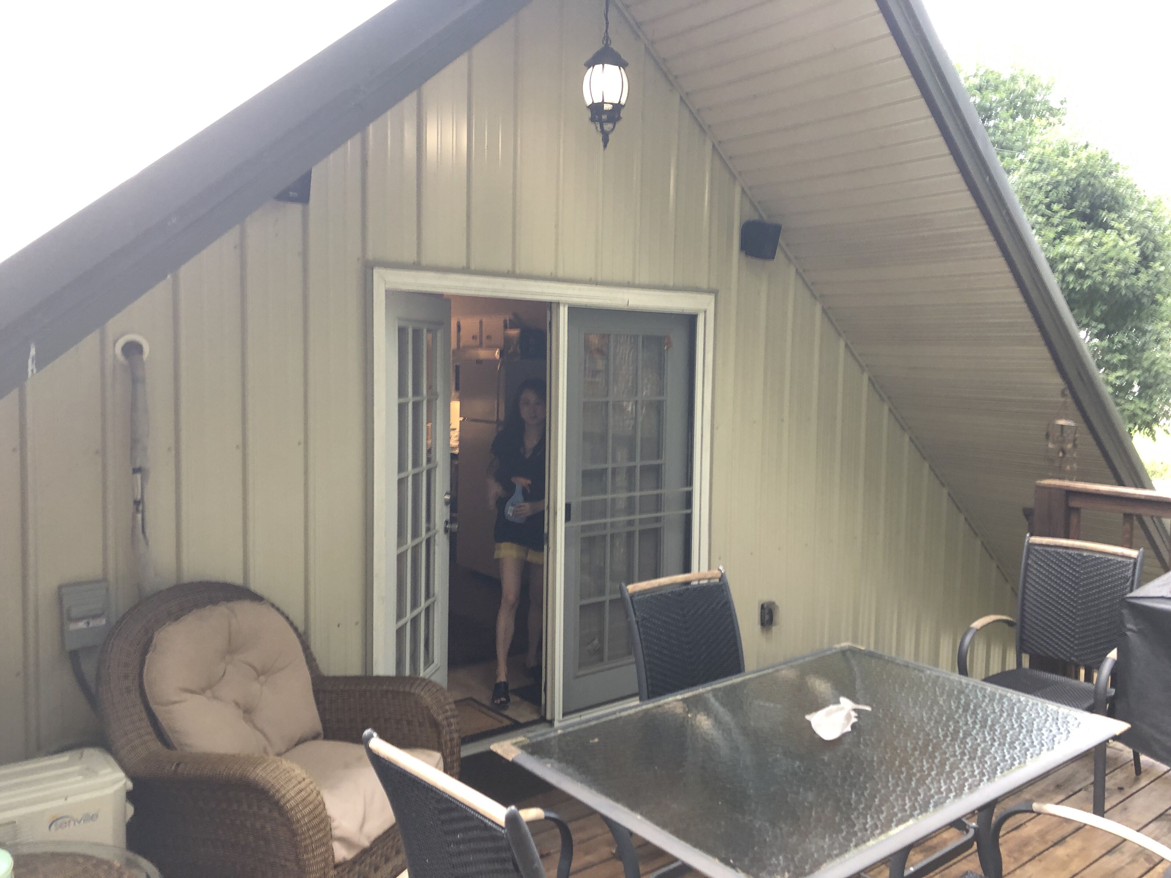 A covered patio area with a glass table, wicker chairs, and a sliding glass door leading to a kitchen.