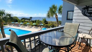 Ein Balkon mit Glastisch und Stühlen, mit Blick auf einen Pool und den Ozean.